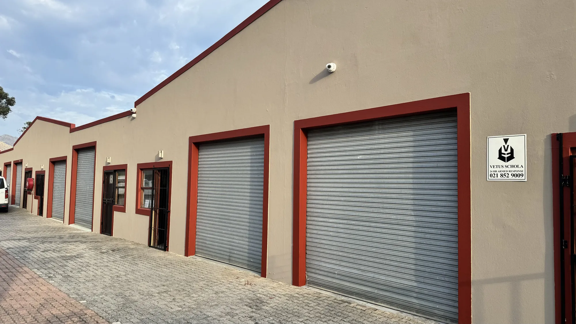 A row of units with red-framed roller doors along the paved yard